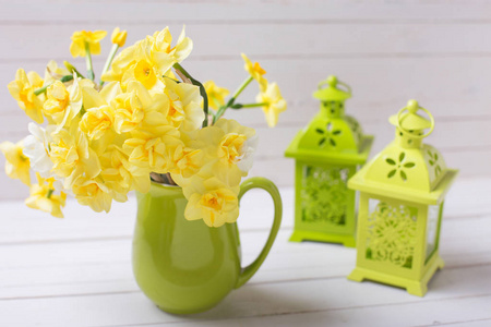 黄色的春天水仙花或水仙花在绿色水罐和装饰绿色灯笼在白色的木制背景。 选择性聚焦。 复活节背景。