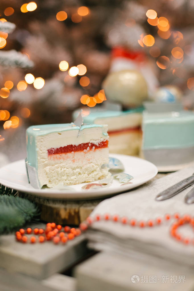 圣诞蛋糕切片配上果冻和蛋酥放在白色盘子里配上冷杉和背景灯