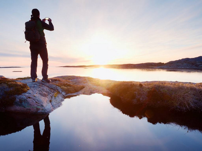 旅行的人在海上采取自拍照后方剪影。旅游与背包站在一块岩石上