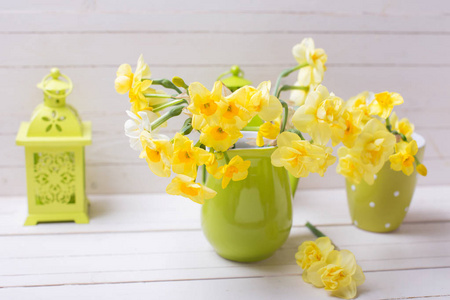 黄色的春天水仙花在绿色花瓶和装饰绿色灯笼在白色的木制背景。