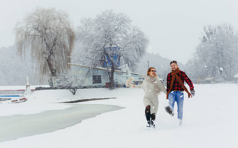 美偶牵手的全长肖像在下雪期间愉快地沿着白雪覆盖的村子散步