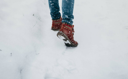 在冬天的公园里，腿女人穿着鞋子在雪地上行走。