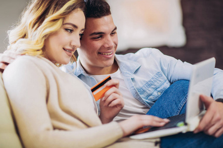 年轻的幸福夫妇坐在家里，用笔记本电脑和信用卡进行网上购物