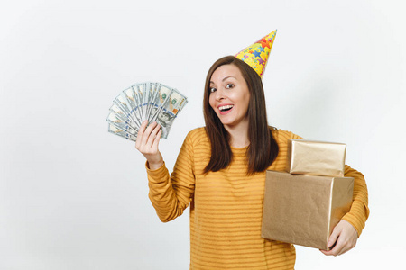 白种人有趣的年轻快乐的女人在黄色的衣服, 生日派对帽拿着礼物和一沓现金的金色礼品盒, 庆祝节日的白色背景隔离广告