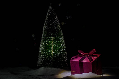 红色圣诞节礼物箱子和冷杉树在雪。圣诞节家庭装饰与雪和树在一个黑暗的背景与复制空间。选择性焦点