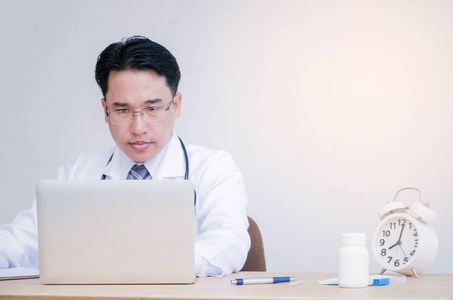 亚洲医生，脖子上戴着听诊器，手提电脑，闹钟，笔，药瓶放在桌子上，医院研究科学，化学，保健，医疗技术概念