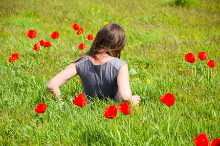 美丽的仙女少女在郁金香花丛中的田野里。 一个女孩在红花和绿色田野背景上的肖像。 郁金香领域。