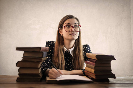 带眼镜的白种人女孩，带着一些书在书桌前学习