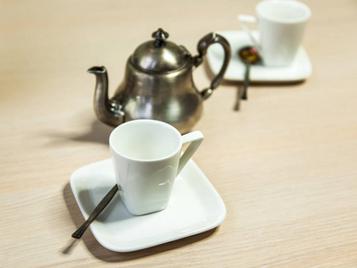咖啡浓咖啡的白瓷杯和一个古老的银咖啡壶在桌子上