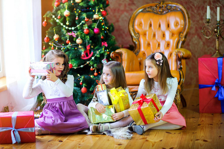 圣诞节早晨，三个姐姐在圣诞树附近的地板上，手里拿着礼物