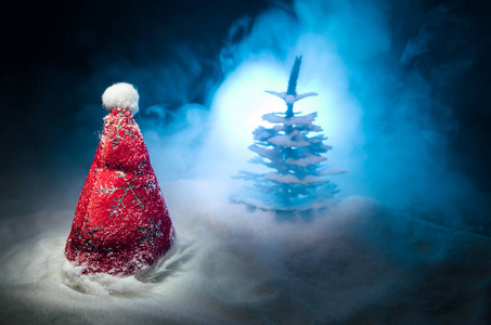 圣诞假期新年背景与圣诞老人的帽子和模糊的圣诞树在白雪皑皑的背景。新年概念形象装饰与假日属性。深色色调背景