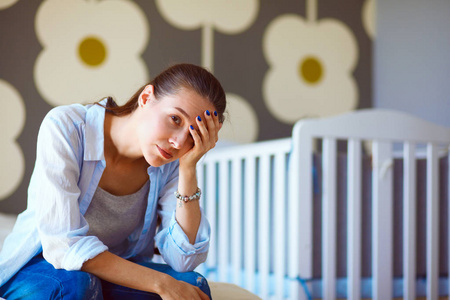 年轻累了坐在附近儿童床床上的女人。年轻的妈妈