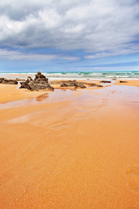 流出过程中沙滩上的大石头条。 黑色和灰色的石头，黄沙和远处的海洋。 晴朗的夏日
