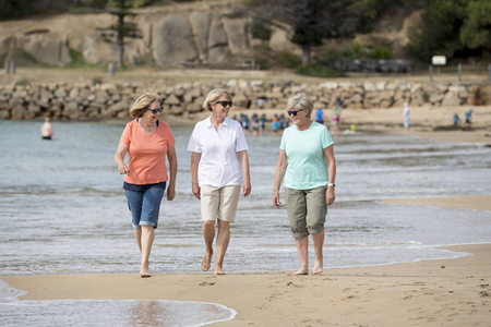 三高级成熟退休妇女小组在他们的60s 有乐趣一起享受一起愉快漫步在海滩微笑嬉戏