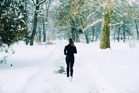 女运动员冬天在公园里慢跑，公园周围有雪。 听音乐和锻炼