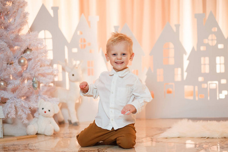 可爱的金发小男孩靠近圣诞玩具纸房子。