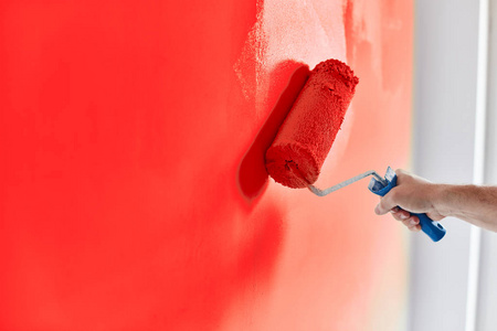 男性手绘墙面漆辊。粉刷公寓, 用红色颜料翻新