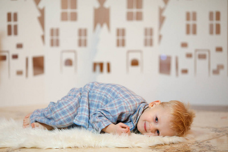 可爱的金发小男孩穿着睡衣靠近圣诞玩具纸屋。
