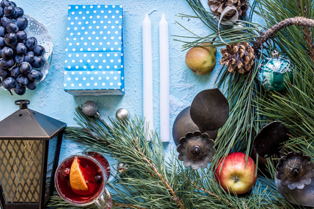 在蓝色背景上有橙色八角豆蔻和肉桂的热的温热的葡萄酒。圣诞树树枝, 礼物和锥体
