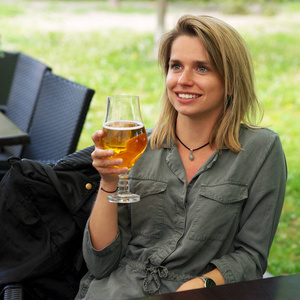 年轻微笑的妇女喝玻璃啤酒在街道餐馆