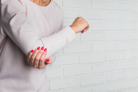 肘部疼痛。 女人用手握住她的胳膊肘。 伤害健康问题手弯曲问题。 光线背景。