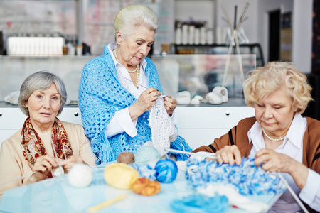三位漂亮的老年妇女聚集在客厅里，热情地为家人编织温暖的衣服