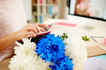 花艺设计师的近景漂亮的蓝白菊花笔记本，五颜六色的包装纸，花店手里拿着数码平板电脑