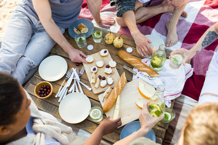 野餐桌上的各种食物和周围的几个朋友吃三明治和水果，喝自制的柠檬水