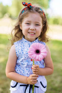 可爱的小女孩的肖像，卷发，头带着粉红色的花，露出牙齿的微笑，看着相机