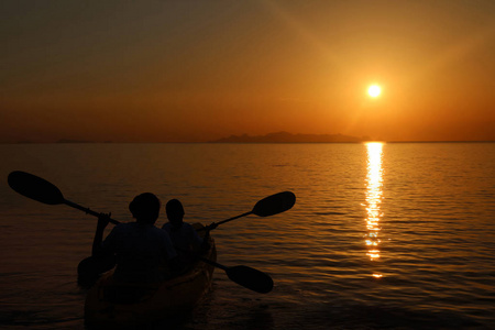 母亲和女儿在日落时在海里划独木舟