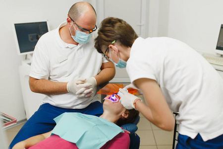 加工的牙齿美白 Uv 灯的光组成。专业的牙医和女助手帮助治疗女性患者的牙齿在诊所光办公室与现代工具设备