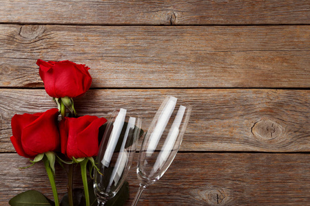 木制桌子上放着一束红玫瑰的香槟酒杯