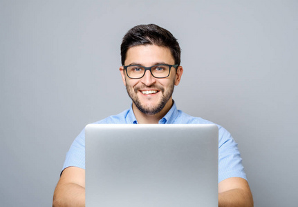 年轻的微笑的人坐在办公桌上的笔记本电脑的肖像