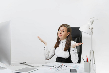 困惑和全神贯注的棕色头发业务妇女在西装和眼镜坐在办公桌上, 在计算机与现代显示器与文件在轻型办公室, 在白色背景的手传播