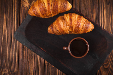刚出炉的羊角面包, 在棕色木制背景下的白杯咖啡杯。法式早餐早餐的新鲜糕点。现代的黑暗情调风格。美味的甜点水平横幅