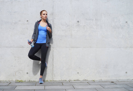 年轻健康和运动的女人站在混凝土水泥墙附近。 健身运动城市慢跑和健康生活方式概念