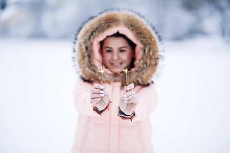在温暖的冬季夹克户外愉快的俏丽的妇女微笑喜欢冬天旅途, 穿着手套和敞篷, 许多雪, 吹的雪到照相机, 闪闪发光的孟加拉灯