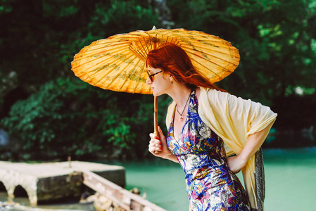 戴眼镜的成年 redhaired 女人在亚洲旅行, 在一个带中国雨伞的公园散步