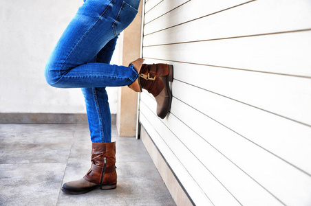 靠在墙上的鞋子时髦的人腿穿着蓝色牛仔裤和棕色皮靴靠在墙上.