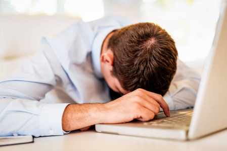 年轻疲惫的商人睡在办公桌上的笔记本电脑前。