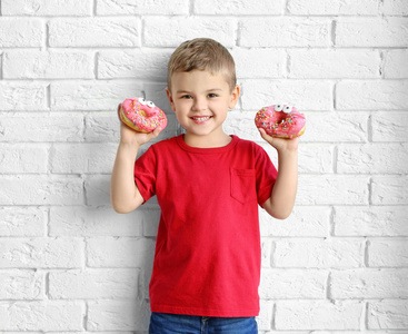 一个小男孩，在白砖墙附近有甜甜的甜甜圈