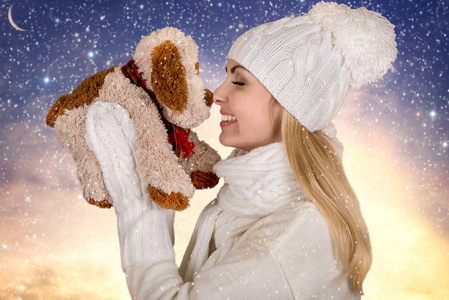 一个年轻女人的肖像，穿着一件漂亮的针织衣服，帽子，围巾和手套，抱着一只玩具狗，象征着新年。