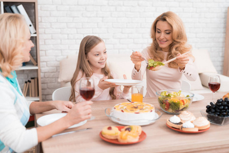 妈妈奶奶和小女孩在家一起吃饭. 他们桌子上有蔬菜和糖果.照片