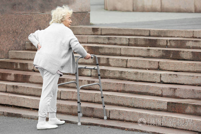 一位带扶手架的老年妇女走上户外楼梯