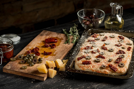 自制比萨饼与橄榄油，奶酪，沙拉米，橄榄在切割板上的木制桌子，复制空间