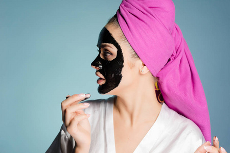 一个有吸引力的女孩在她的头上用粉红色的毛巾涂抹在她的脸上的黑色清洁面具