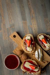 碗与水果果酱和美味的三明治与草莓，坚果，奶酪在木板顶部，复制空间