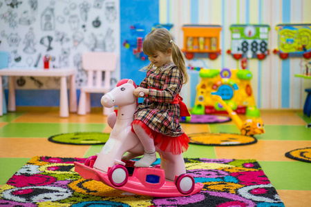 喜笑颜开的小姑娘骑着木马荡秋千.有趣的孩子在游戏室玩照片