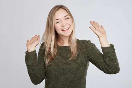 穿着绿色休闲毛衣,打招呼,挥动双手,带着牙齿的微笑照片