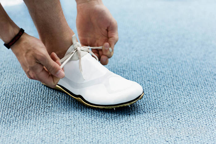 男跑运动员在蓝色地毯上系鞋带的裁剪图像